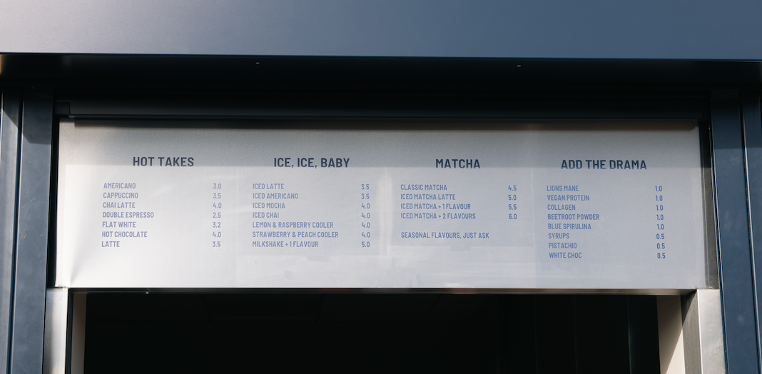 Person ordering at a 'scene at stride' food stand with a menu board above.